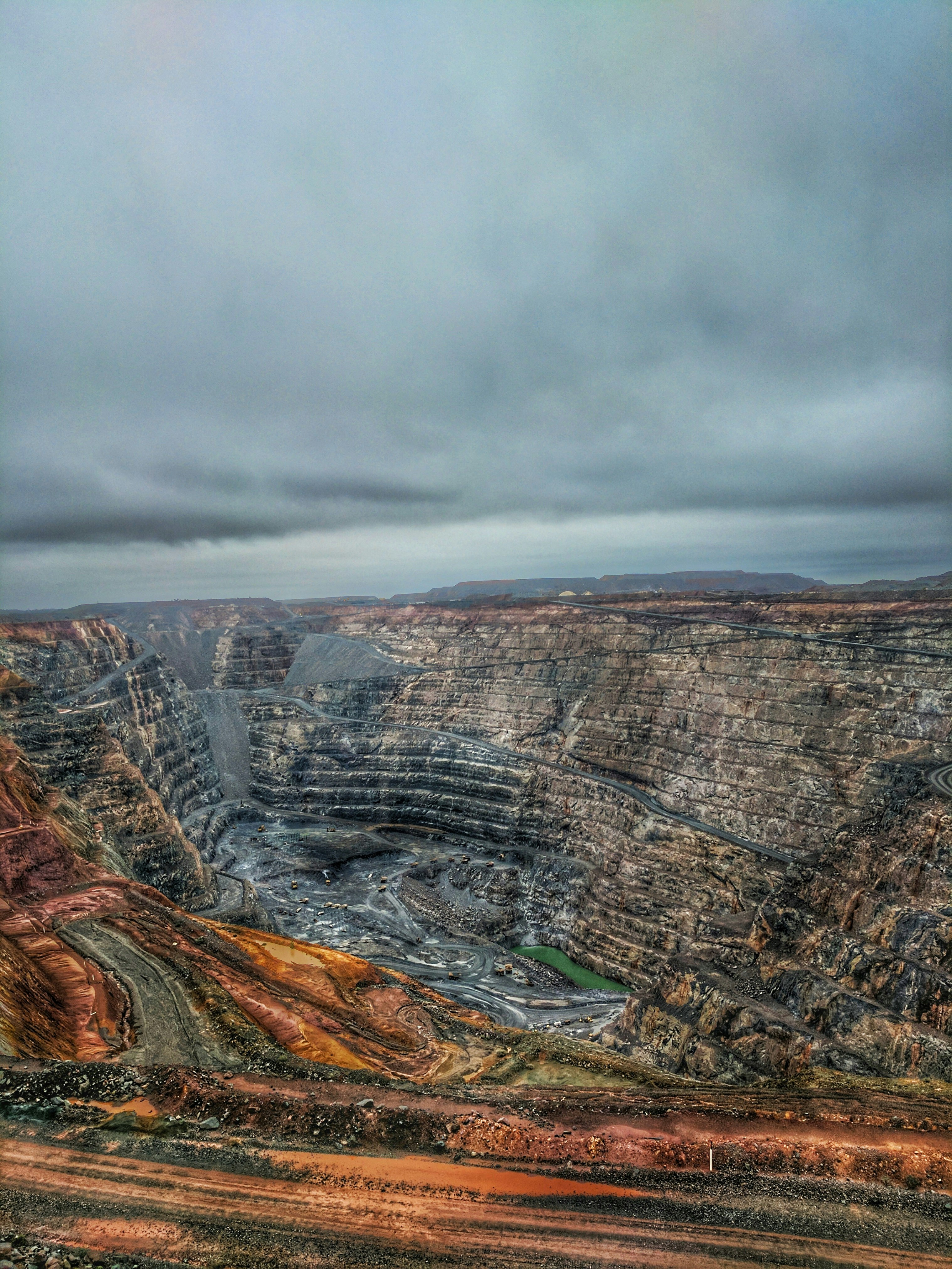 Terraced walls of a large open-pit mine under a cloudy sky
